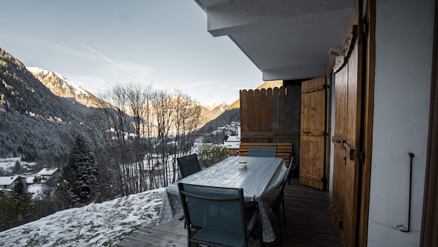Un área de comedor al aire libre con mesa y sillas, con vistas a un paisaje nevado y montañas.
