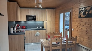 Cocina compacta con armarios de madera, un microondas negro y un lavamanos. Hay una mesa de comedor con sillas y una ventana con vistas al exterior.