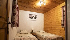 Una habitación acogedora con paredes y techo de madera, que presenta dos camas con ropa de cama escocesa, una mesita con una lámpara y un cuadro en la pared.