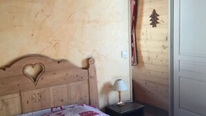 Une chambre à coucher avec une tête de lit en bois ornée d’un motif en forme de cœur, une courtepointe à motifs de cœur, une lampe de chevet et une porte avec un panneau en bois.
