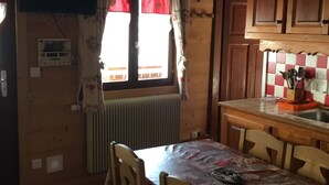 Une cuisine compacte avec des meubles en bois, une table à manger avec des chaises, un radiateur et une fenêtre avec des rideaux rouges.