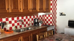 Une cuisine avec des meubles de rangement en bois, un crédence à carreaux, une cuisinière à gaz, une machine à café et une table à manger avec des chaises.