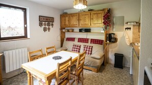 A compact kitchen with wooden cabinets, a dining table with chairs, a small sofa, and a window with blinds. - Châtel Apartment 4 pax, Pets allowed, Balcony, Parking (Châtel)