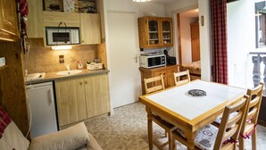 A compact kitchen with wooden cabinets, a microwave, a sink, and a dining table with chairs. - Châtel Apartment 4 pax, Pets allowed, Balcony, Parking (Châtel)