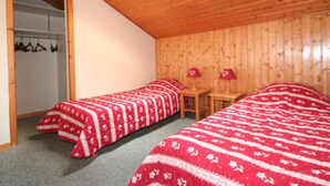 Een kamer met twee bedden, houten wanden, een inloopkast met hangende kleding en een dakraam.