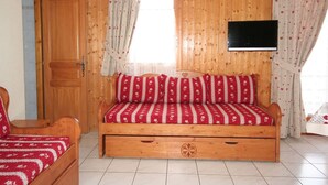Een kamer met houten vloeren, een bed, een televisie en een raam met gordijnen.