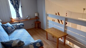 A cozy room with a wooden floor, a blue patterned sofa, a small wooden table, and a white railing with hanging decorations. - 2-room apt for 5 people in Châtel with south-facing balcony (Châtel)