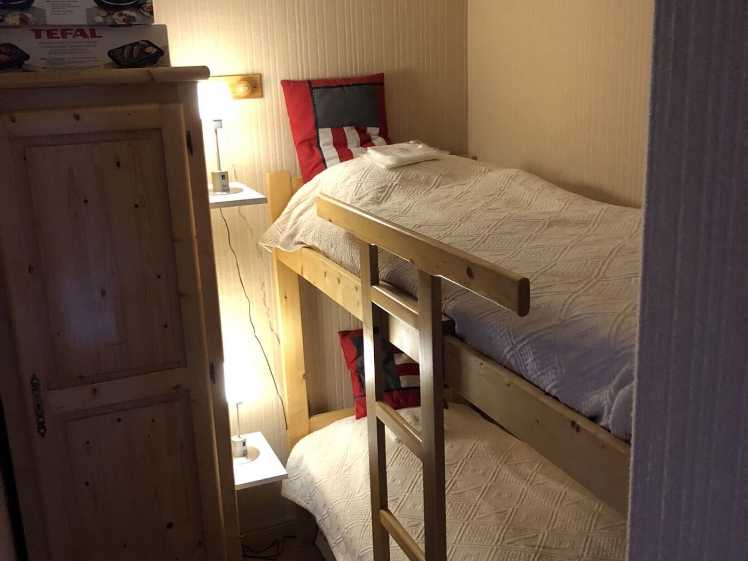 A bunk bed room with a wooden wardrobe and a small bedside table.