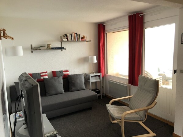 A compact living room with a grey sofa, a wooden chair, a TV, and a bookshelf. - 2-room apartment in Châtel, 5 people, with south-facing terrace (Châtel)
