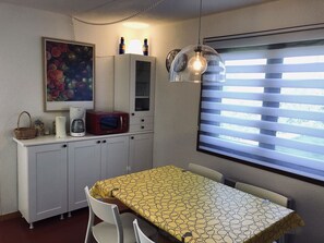 A compact kitchenette with a microwave, coffee maker, and a painting. There is a table with a yellow patterned tablecloth and a window with blinds. - 2-room apartment in Châtel, 5 people, with south-facing terrace (Châtel)