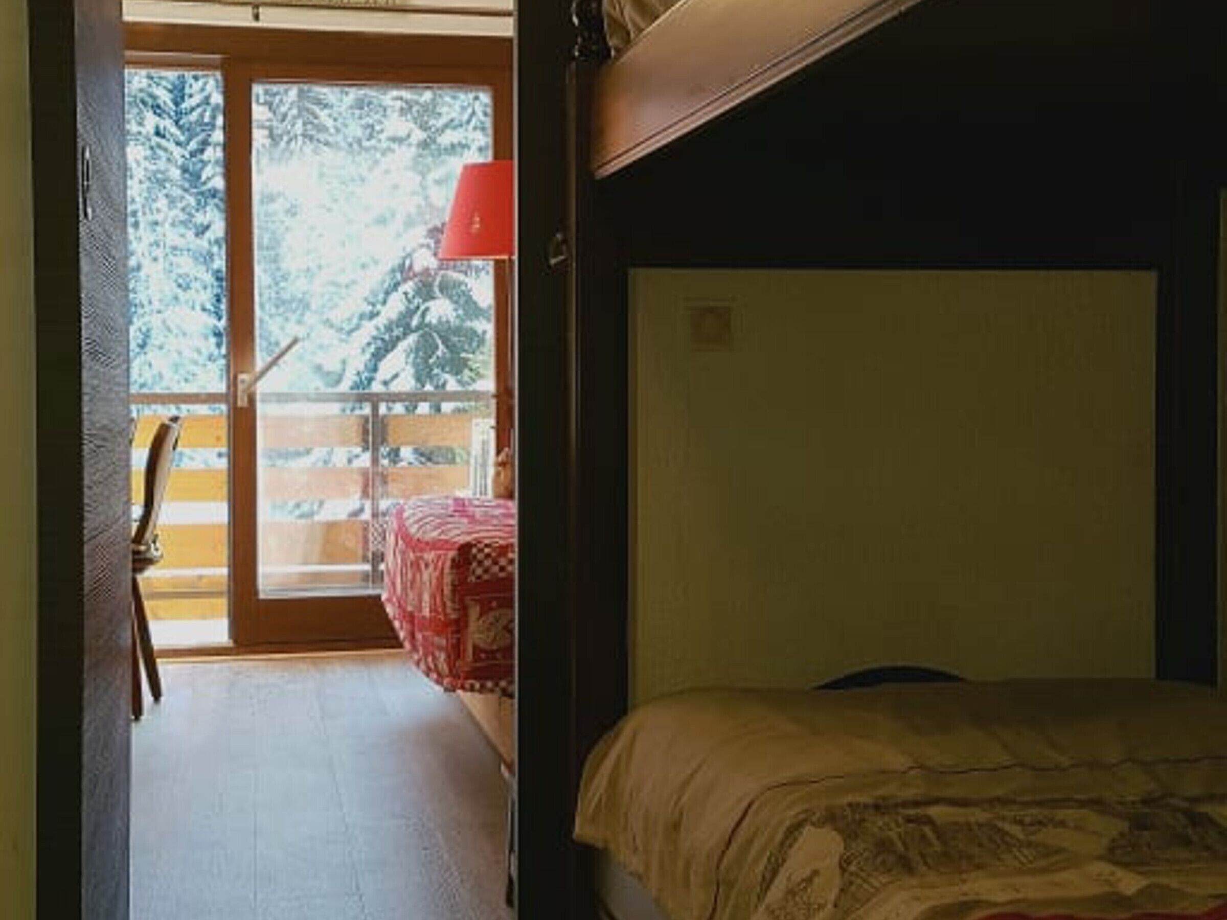 Ein Zimmer mit einem Bett, einer roten Lampe und Blick auf verschneite Bäume durch eine Glasdoor.