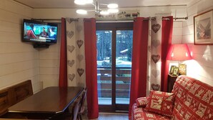 A cozy living room with a television, a sofa, a dining table, and a view of a snowy landscape through the window.