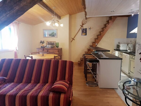 A cozy living area with a striped sofa, a dining table, and a kitchen with a wooden staircase. - 2-Room Apartment 52 m² for 4-5 guests (Cauterets)
