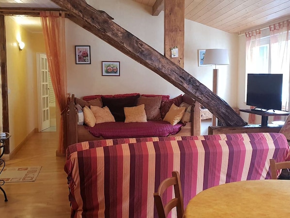 A cozy room with a wooden ceiling beam, a sofa with cushions, a television, and a striped tablecloth.