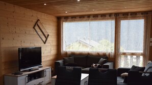 Ein gemütliches Wohnzimmer mit Fernseher, Sofa und Essbereich.