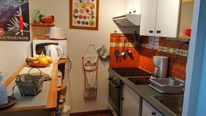 A compact kitchen with a microwave, toaster, and sink. There is a fruit basket and a hanging apron on the counter.