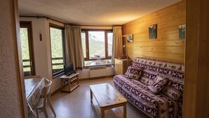A cozy room with a wooden sofa, a small table, a TV on a stand, and a window with curtains.