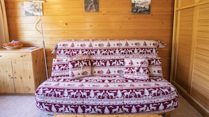 A cozy room with a wooden wall, a bed with patterned bedding, a small wooden dresser, and two framed pictures on the wall.