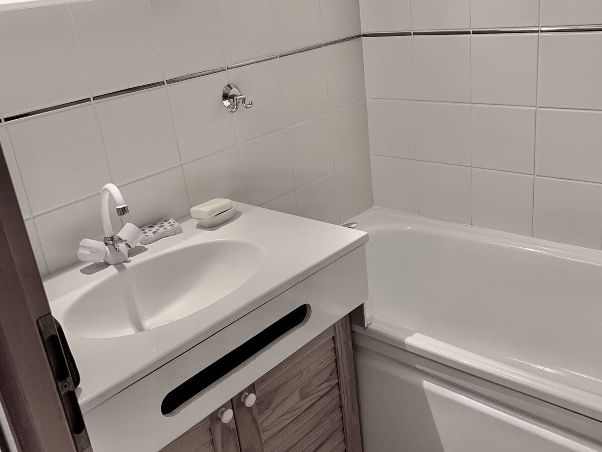 Ett badrum med ett vitt handfat, en blandare, en tvålkopp och ett badkar.