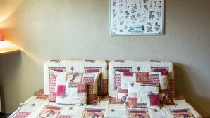 A bed with a patterned bedspread and pillows, a wall-mounted botanical illustration, and a bedside lamp. - Cozy Studio for 3 with Terrace, Steps from Petit-Châtel Ski Lift (Châtel)