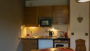 A compact kitchen with wooden cabinets, a microwave, a sink, and a small refrigerator. - Cozy Studio for 3 with Terrace, Steps from Petit-Châtel Ski Lift (Châtel)