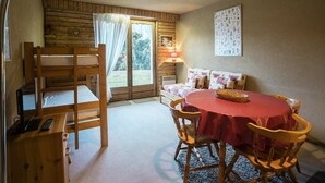 A cozy room with a wooden bunk bed, a dining table with chairs, a lamp, and a window with curtains. - Cozy Studio for 3 with Terrace, Steps from Petit-Châtel Ski Lift (Châtel)