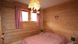 Una habitación de cabaña de madera con una cama, una mesita y una ventana con cortinas a cuadros.