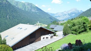 A mountain lodge with a sloped roof, a parking area, and a view of surrounding mountains. - Cozy 2BR Apartment, South-Facing Terrace, Ski Access, WiFi, Parking, 4 Guests (Châtel)
