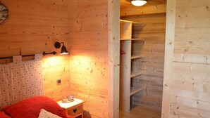 A cozy wooden room with a bed, a nightstand, a wall-mounted lamp, and a wooden closet. - Cozy 2BR Apartment, South-Facing Terrace, Ski Access, WiFi, Parking, 4 Guests (Châtel)