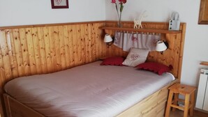 A wooden bed with a headboard, two bedside lamps, a small wooden stool, and a vase with flowers.