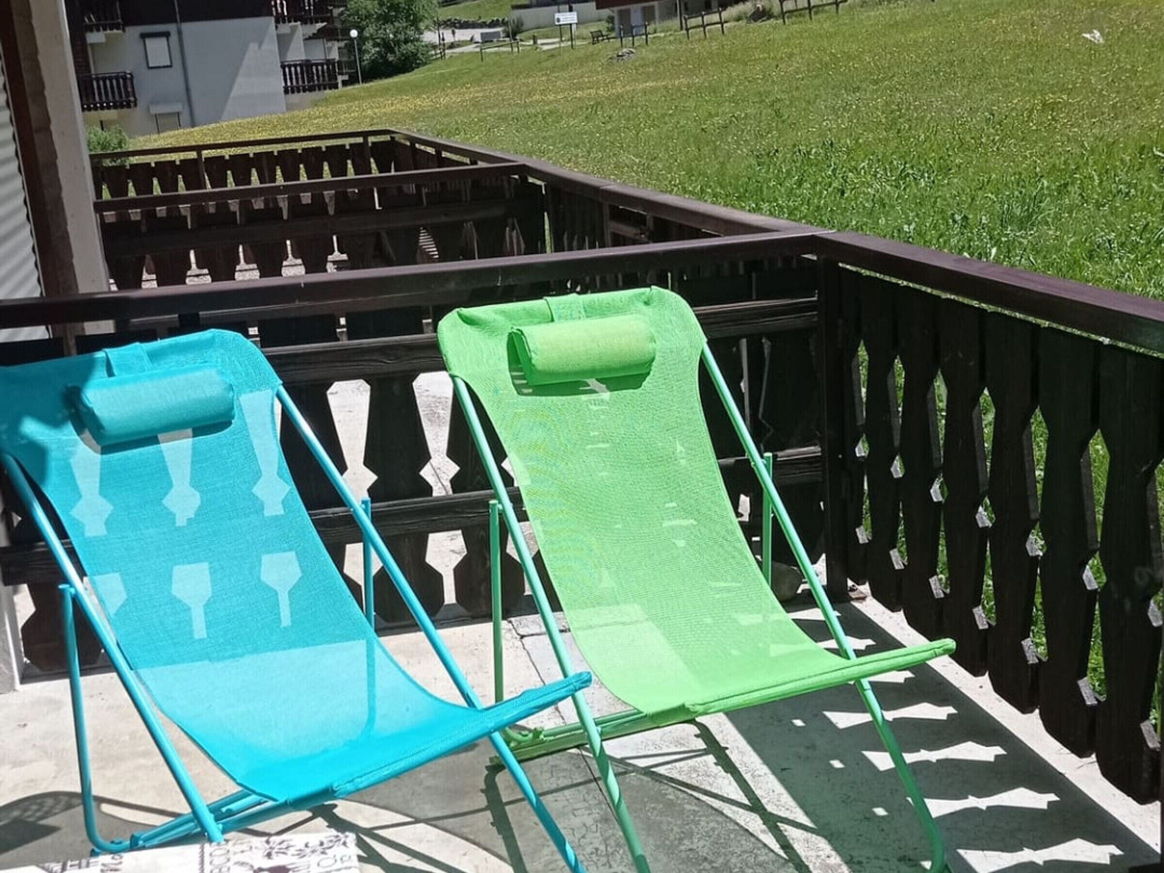 Two outdoor chairs on a balcony with a view of a grassy area and buildings in the background.