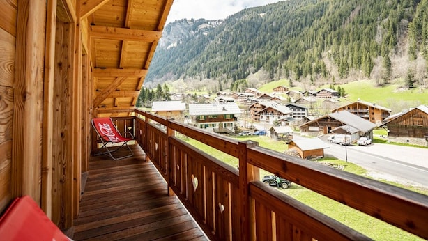A wooden balcony with a view of a mountain village and a road. - Spacious Chalet in Châtel, 8 bedrooms, jacuzzi, near slopes (Châtel)