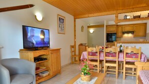 Ein gemütliches Wohnzimmer mit Fernseher, Holzmöbeln, einem Esstisch mit Stühlen und einer Küchenzeile.