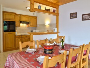 A cozy kitchen with wooden cabinets, a built-in oven, and a dining table set for four with a red tablecloth.