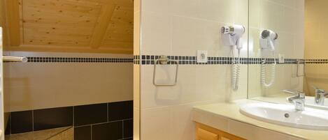 A bathroom with a wooden ceiling, a white sink, a mirror, and a shower area with black and beige tiles.