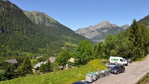 A parking lot with cars and a white van, surrounded by green hills and mountains. - Châtel Apartment 4 ppl, balcony, parking, pets allowed (Châtel)