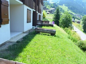 Ein Gebäude mit weißer Fassade, Holzläden und einem Balkon mit Blick auf einen grünen Hügel mit Häusern im Hintergrund.