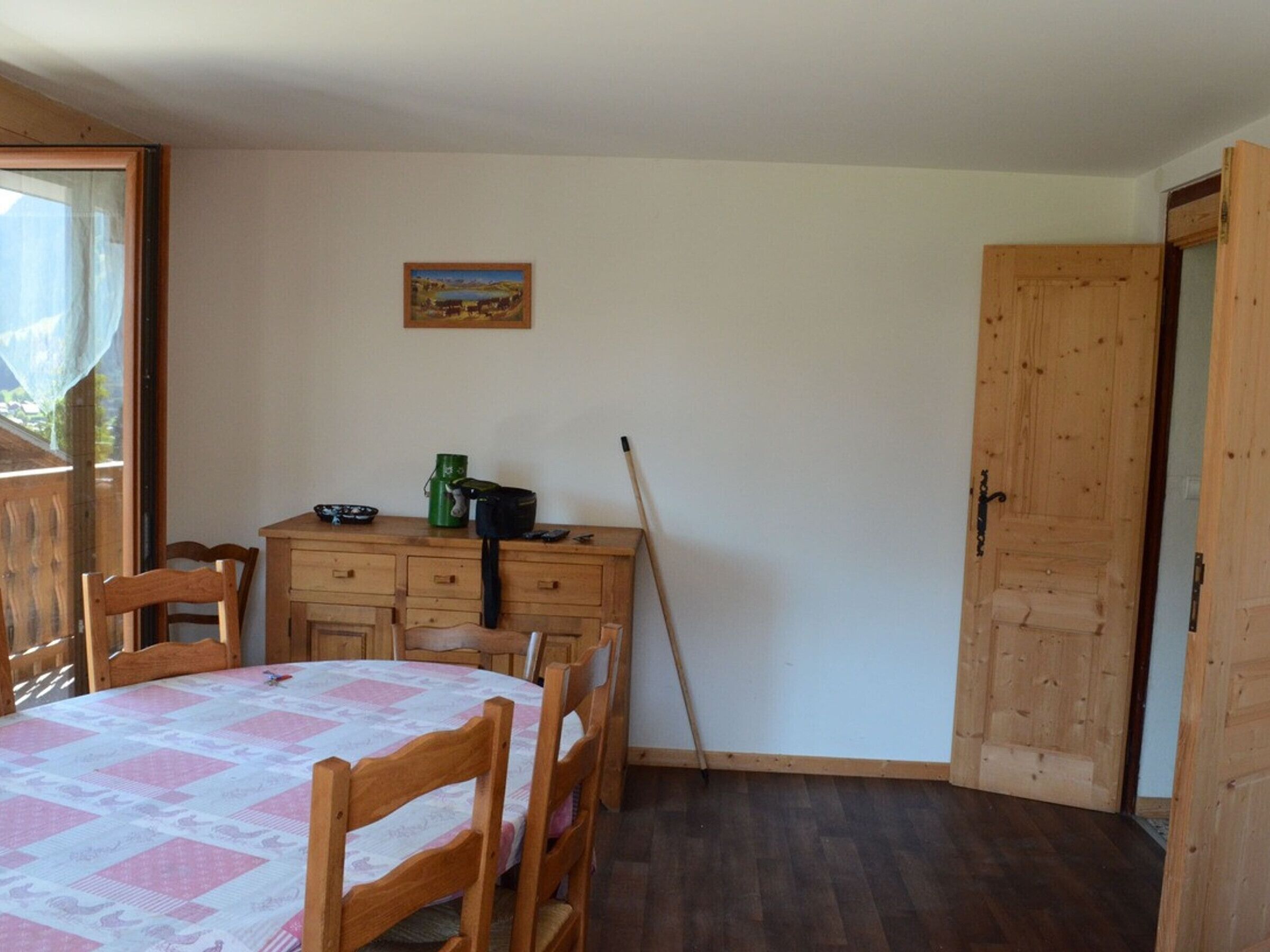 A room with a wooden table and chairs, a painting on the wall, and a door.