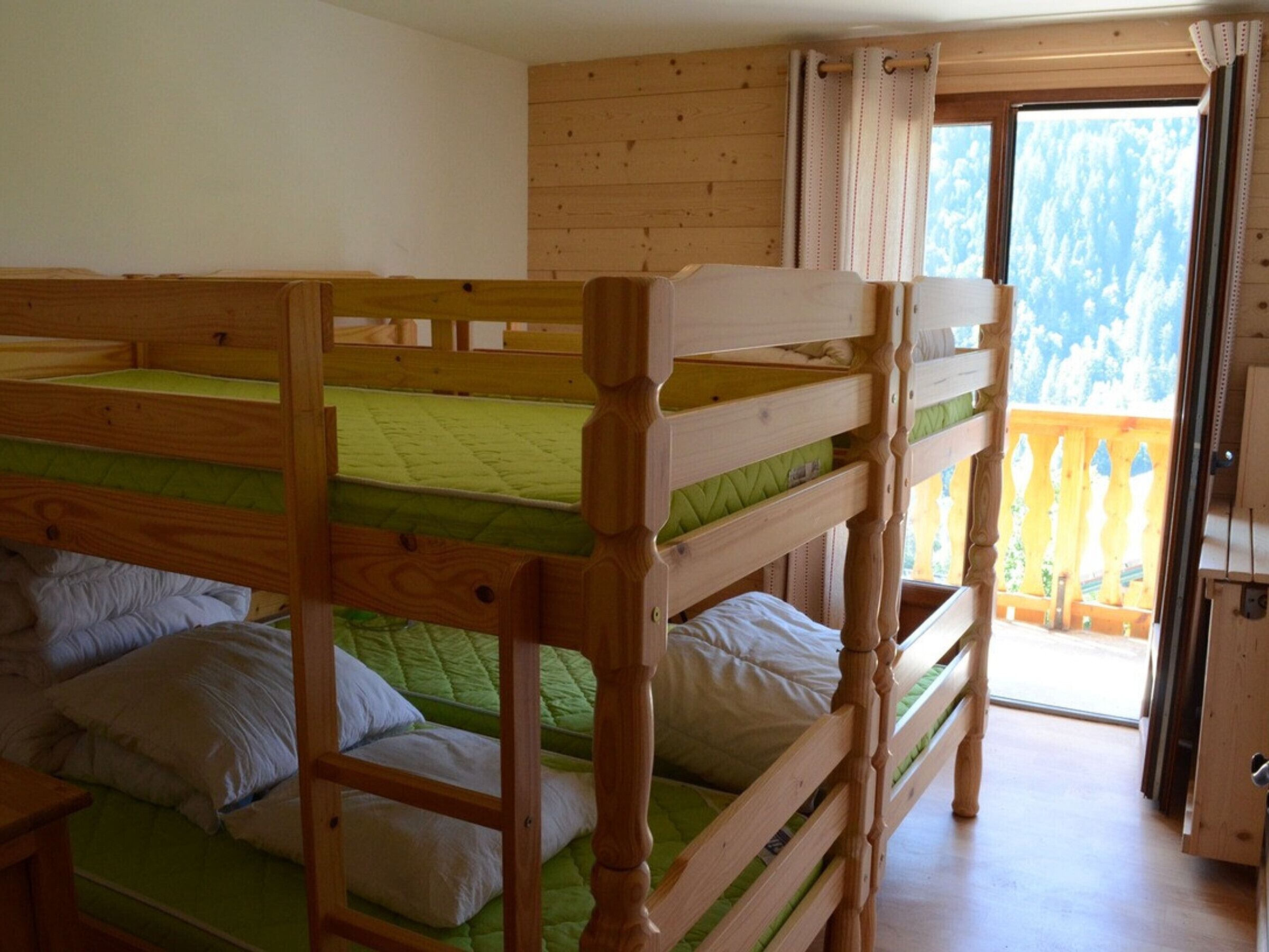 A room with two bunk beds, wooden walls, a balcony with a wooden railing, and a door leading outside.