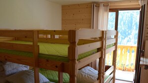 Quarto com duas beliches, paredes de madeira, uma varanda com guarda-corpo de madeira e uma porta que dá para o exterior.