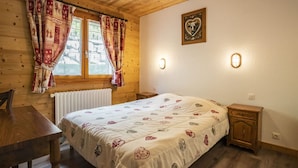 Una habitación de cabaña de madera con una cama, una mesa y un ventanal con cortinas.