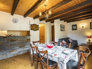 Uma área de refeições com parede de pedra, vigas de madeira no teto, um lustre e uma mesa de jantar posta para quatro pessoas.