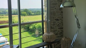Una habitación con un amplio ventanal corredizo que da a un paisaje verde, una lámpara de pie, cestos de mimbre y un libro de 'Picasso' sobre un banco.