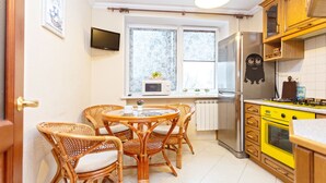 A compact kitchen with a dining area, featuring a refrigerator, oven, and a small window with curtains. - Comfortable apartment (Minsk)