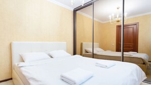 A hotel room with a large mirror, a bed with white linens, a wooden door, and a chandelier. - Comfortable apartment (Minsk)