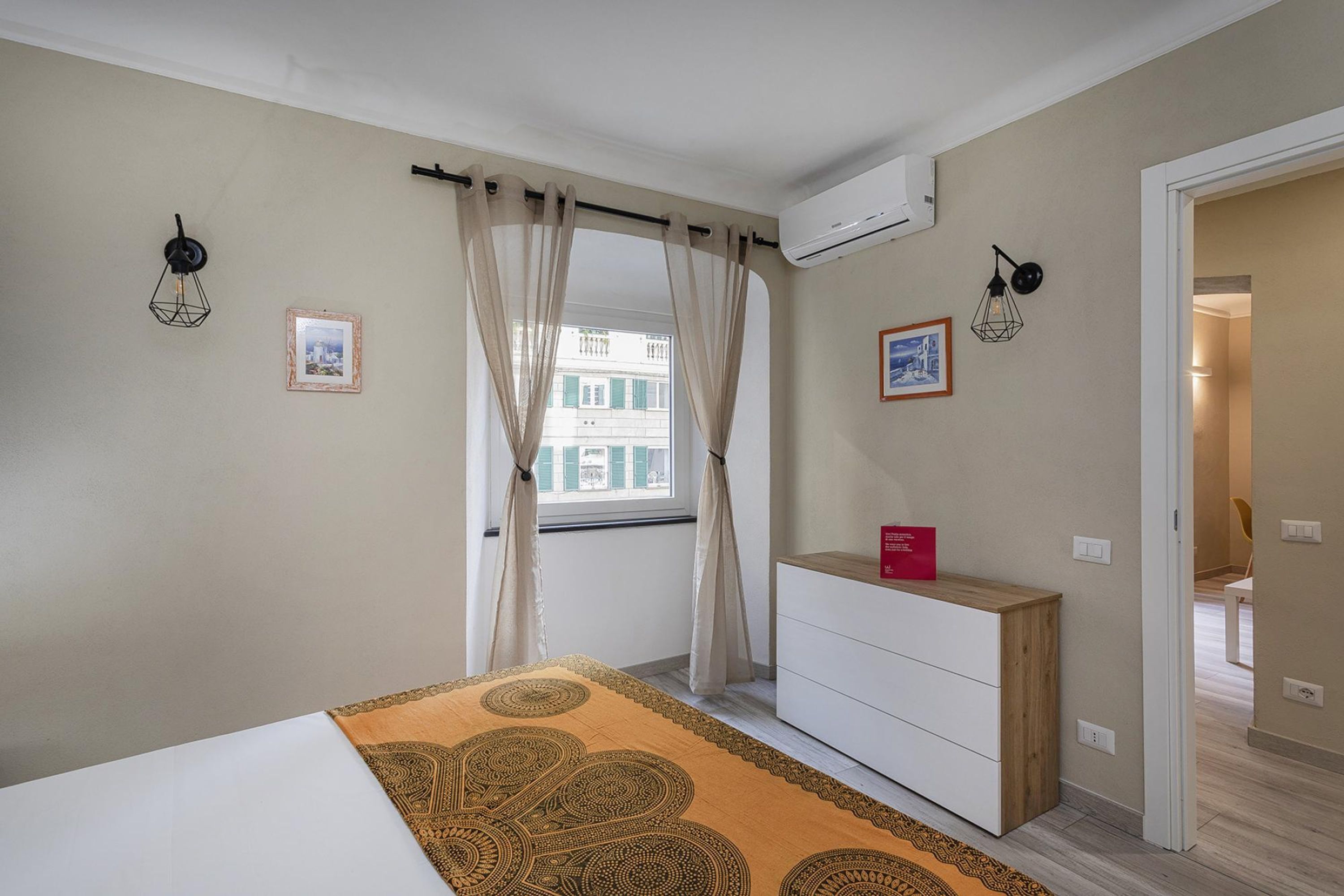 Een slaapkamer met een bed, een dressoir, een raam met gordijnen en twee wandlampen.
