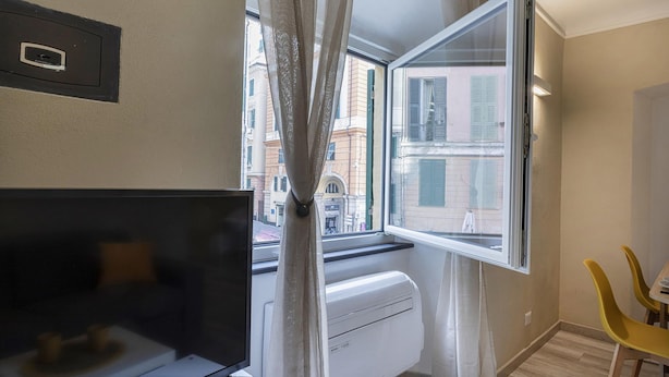 A room with a TV, a window with curtains, a radiator, and a yellow chair. - Raibetta Apartment by Wonderful Italy (Genoa)
