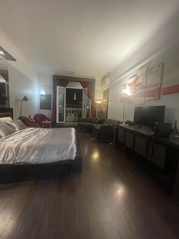 A hotel room with a bed, a desk, a TV, and a balcony with a view of the city.