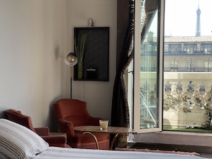 Enjoy a view of the Eiffel Tower from the large window in this stylish room, featuring a comfortable seating area and a cozy bed with striped bedding.