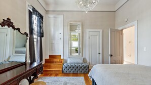 Un dormitorio con una cama grande, un aparador de madera, un espejo, una araña y una escalera que lleva a un balcón.